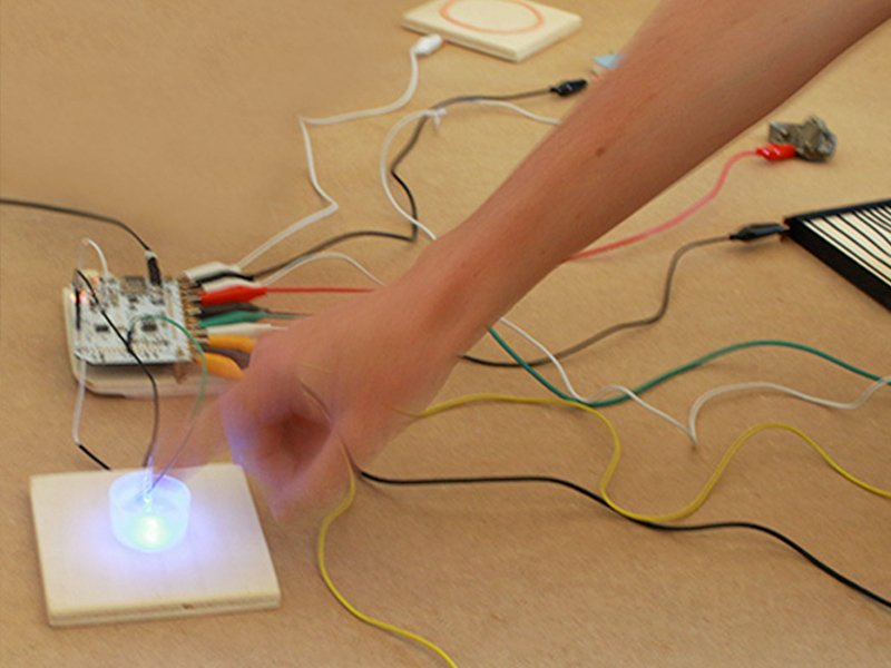 Une main touche une surface interactive qui s'allume, reliée à une carte électronique