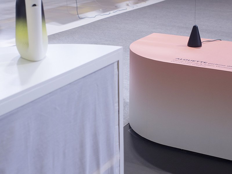 Mobilier du stand en dégradés blanc et rose, avec une carafe Pan et une lampe