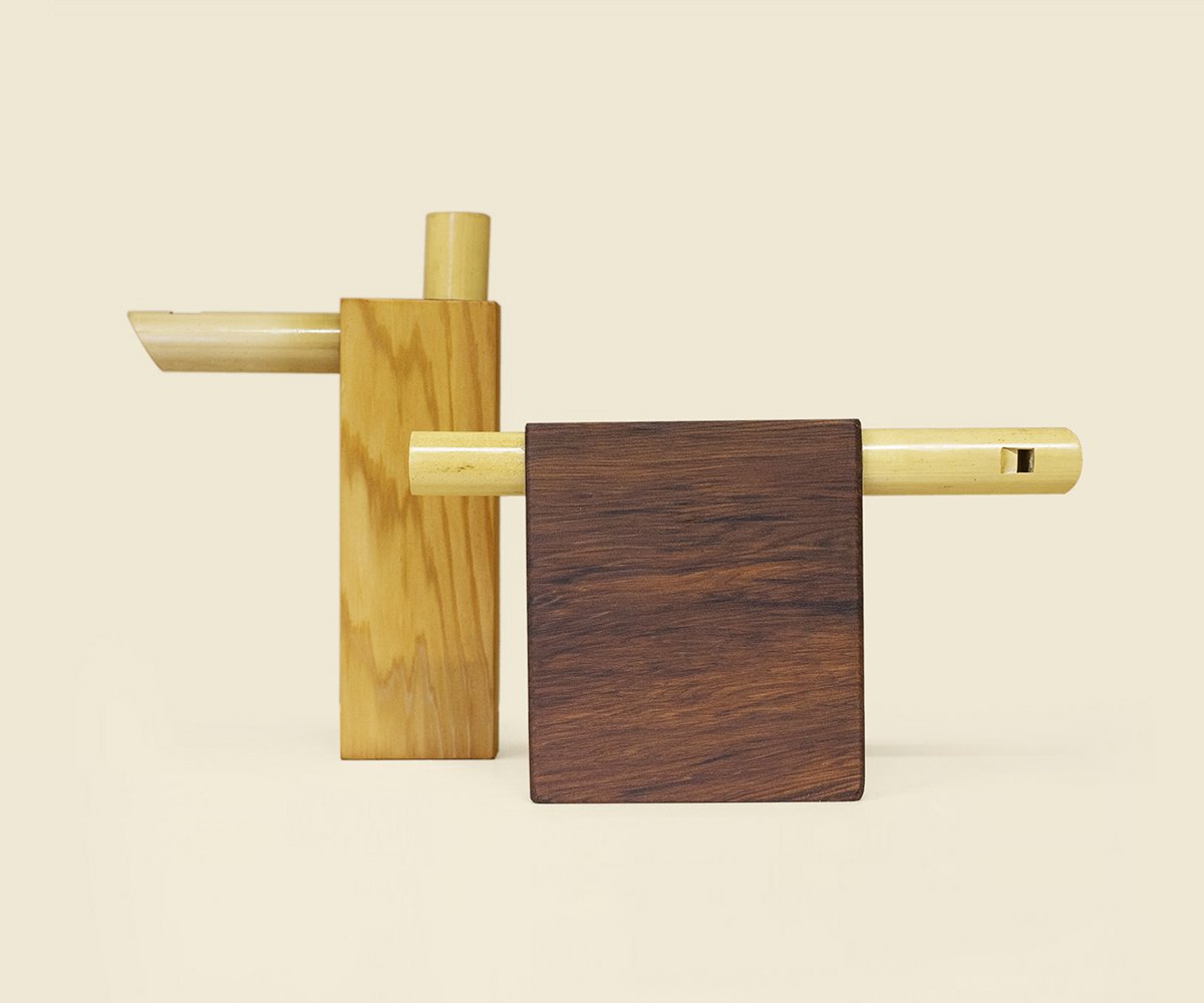 Two Compact flutes: bamboo tubes running through a light wood block and a red cedar block